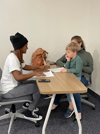 2 adults and 1 child sitting around a table doing a class assignment