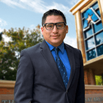 Headshot of University of Texas at Arlington employee Manuel Alonso. The background shows a UTA campus sign.