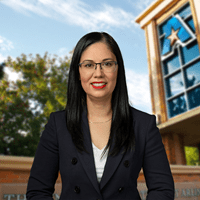 Headshot of University of Texas at Arlington employee Claudia Monreal-Torres. The background shows a UTA campus sign.