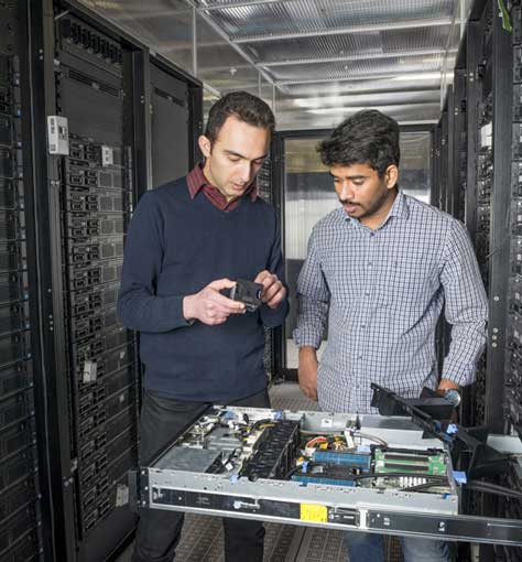 Two researchers examining some electronics in a datacenter.