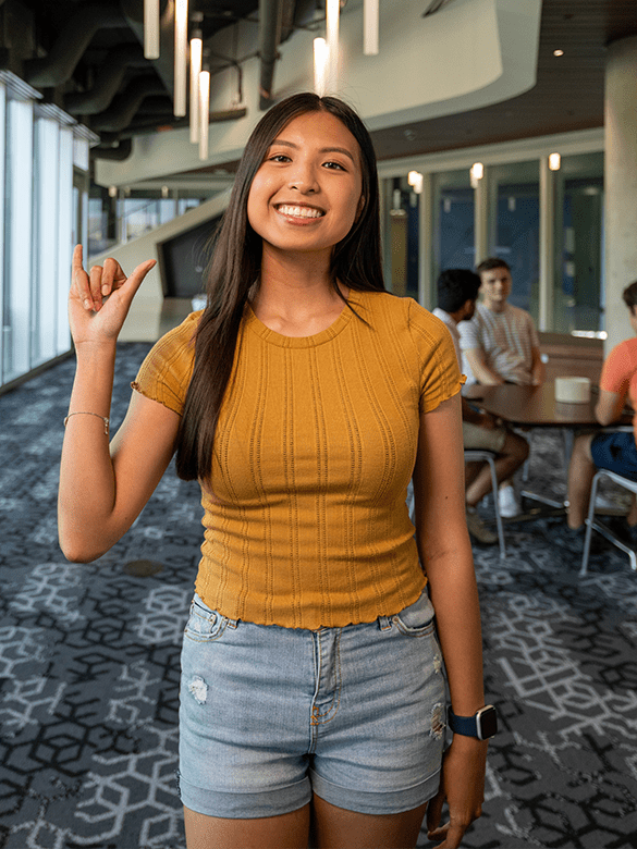 A woman in a yellow top giving the U T A hand sign