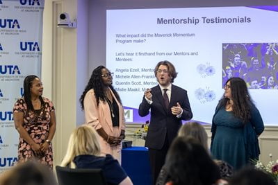 three women and a male speaker talking to a crowd of mentees