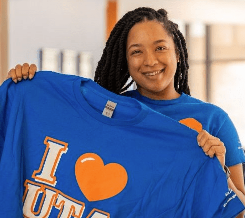 african american woman holding a blue university of texas at arlington t shirt with the words I heart U T A