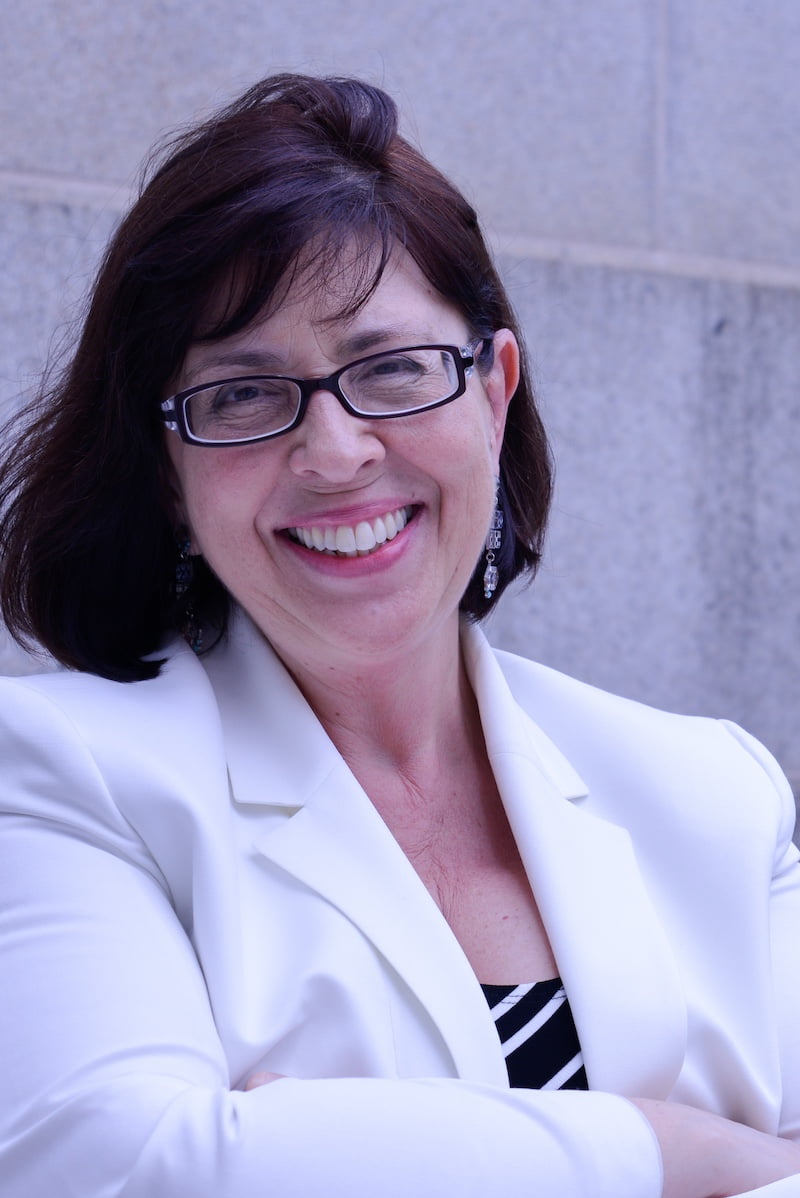 photograph of a woman in glasses with a white suit jacket smiling