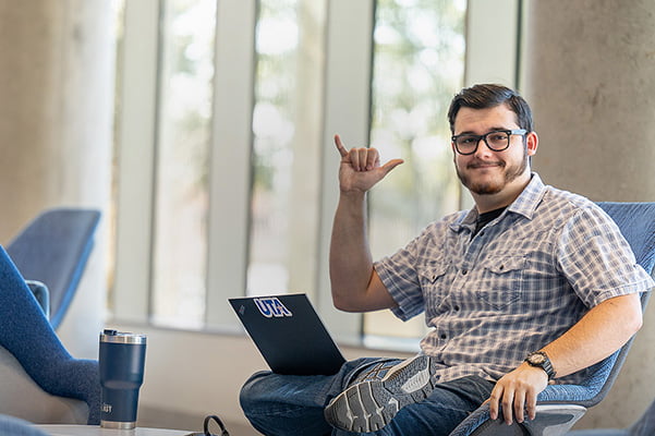 Student with laptop and mavs-up hand sign