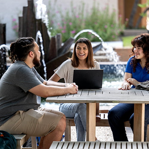 three people sitting outdoors at a picnic table