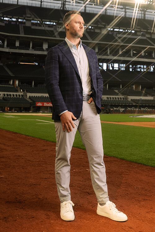 A man in a suit standing on the warning track of a baseball field
