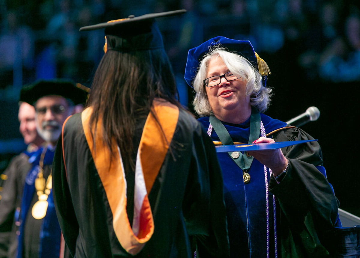 Dean Elizabeth Merwin handing a diploma to a graduating student at the 2019 nursing commencement ceremony