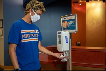 UTA student wearing a mask and using a hand sanitizer dispenser