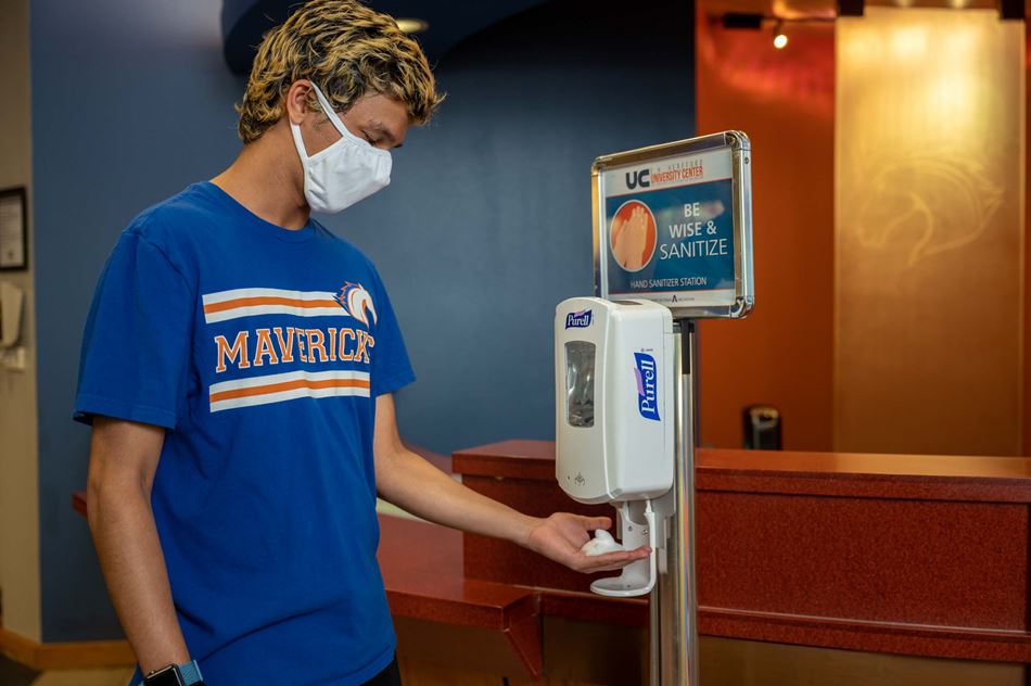 UTA student wearing a mask and using a hand sanitizer dispenser
