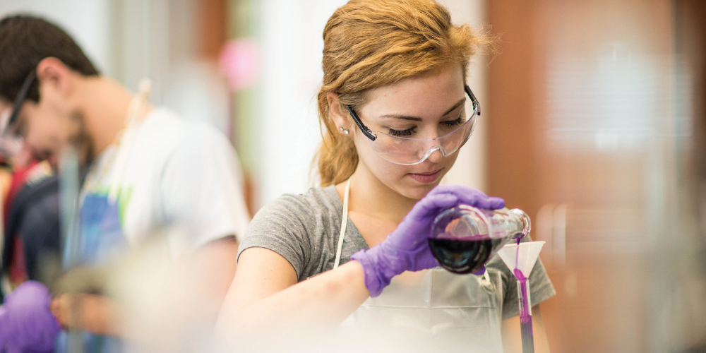 A young student researcher mixes liquids in a chemical lab.