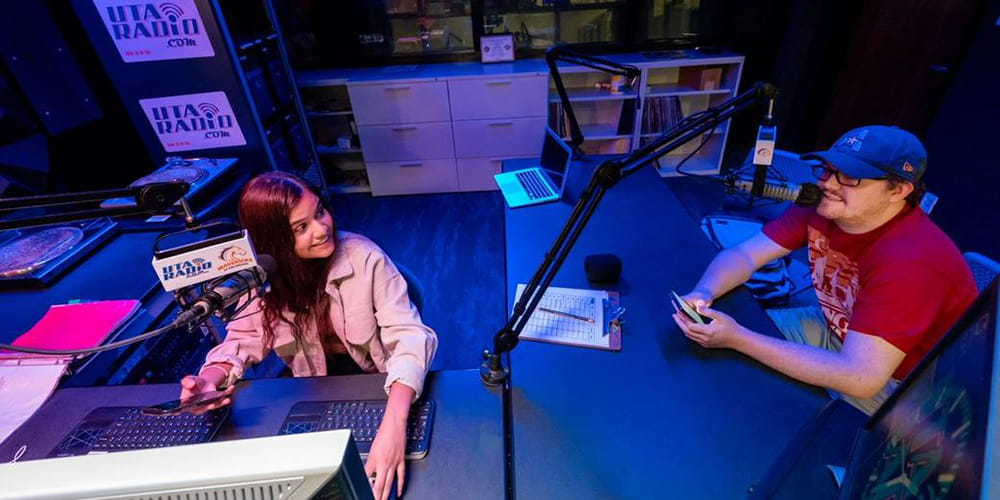 Two students talk on-air in the darkened studio of UTA radio. 