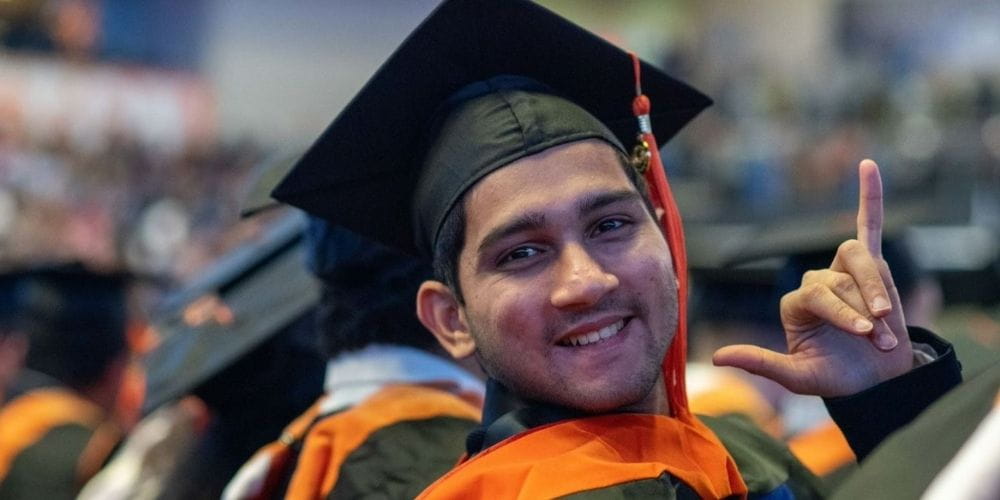 Student graduating in gap and gown gives UTA salute." _languageinserted="true