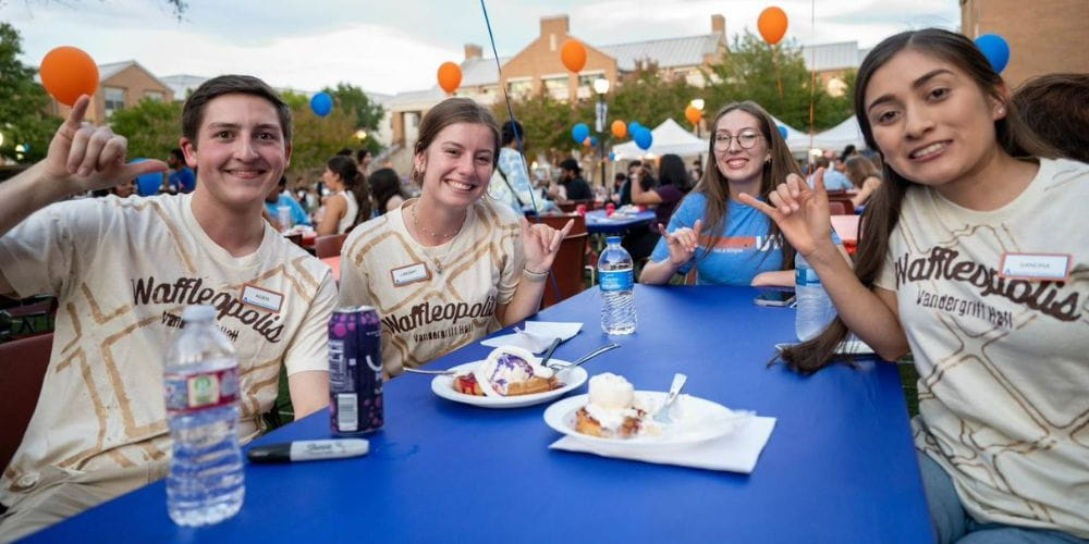 Group of four students in Waffleopolis shirts enjoy waffles during 2022 Waffleopolis event" _languageinserted="true