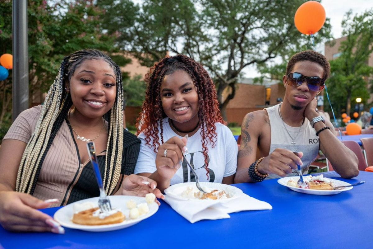 Group of three students sit at table and enjoy waffles at 2022 Waffleopolis event