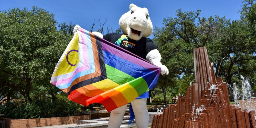 UTA mascot Blaze poses with pride flag on campus." _languageinserted="true