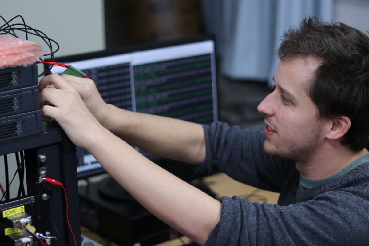 Benjamin Smithers touches wires on a computer in the laboratory at Chiba University." _languageinserted="true