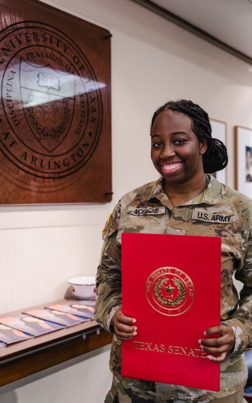 Destiny Moragne standing next to the UTA seal and holding a red folder
