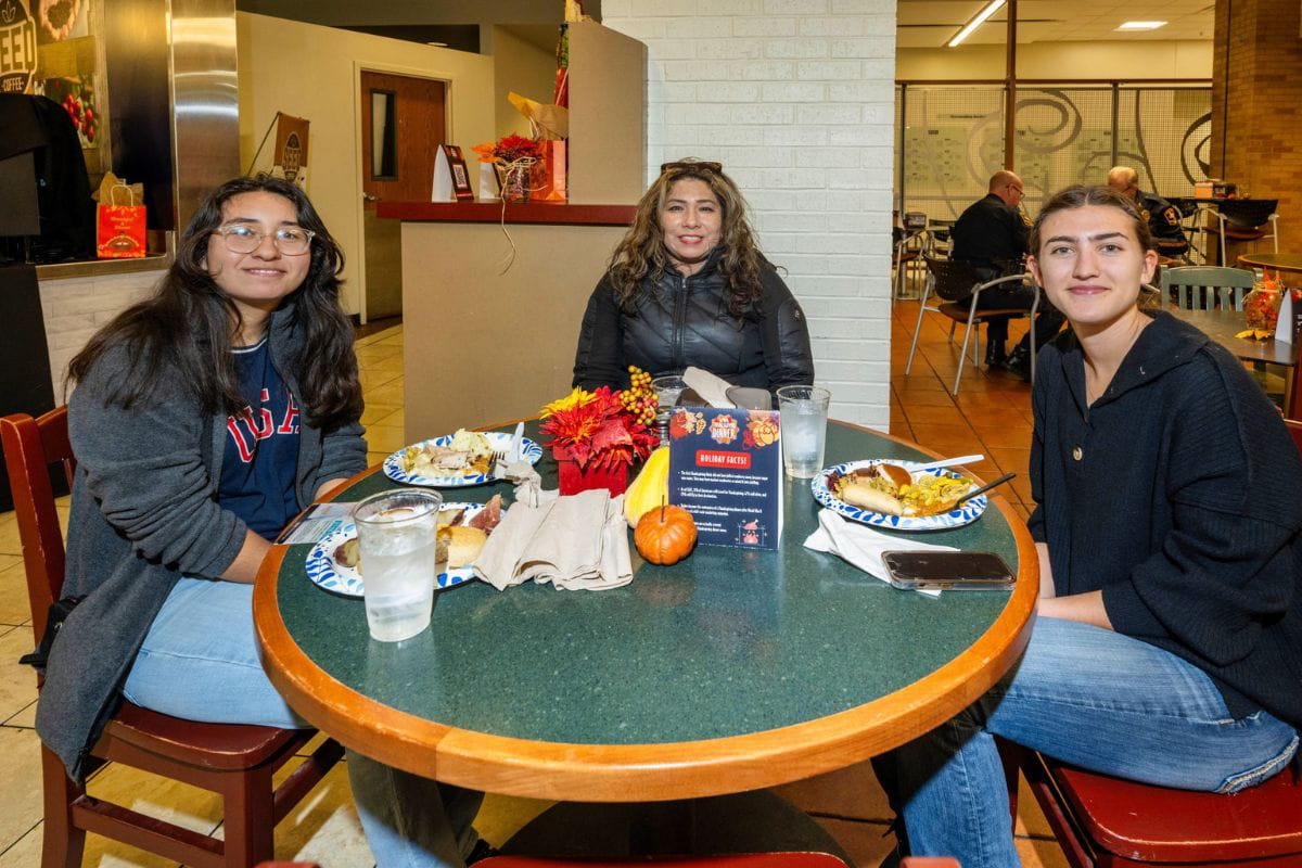 Three students seated at the UTA Thanksgiving dinner