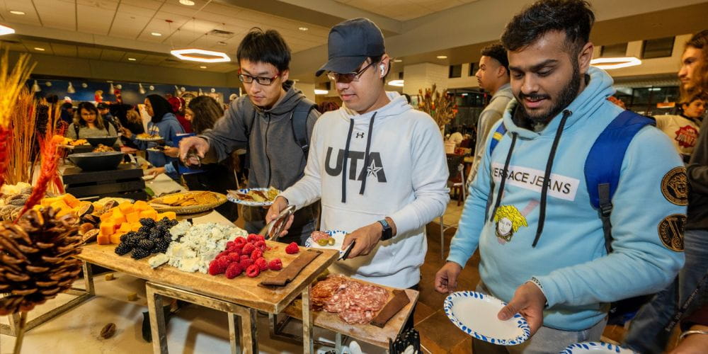 Three students grabbing food at the UTA Thanksgiving dinner" _languageinserted="true