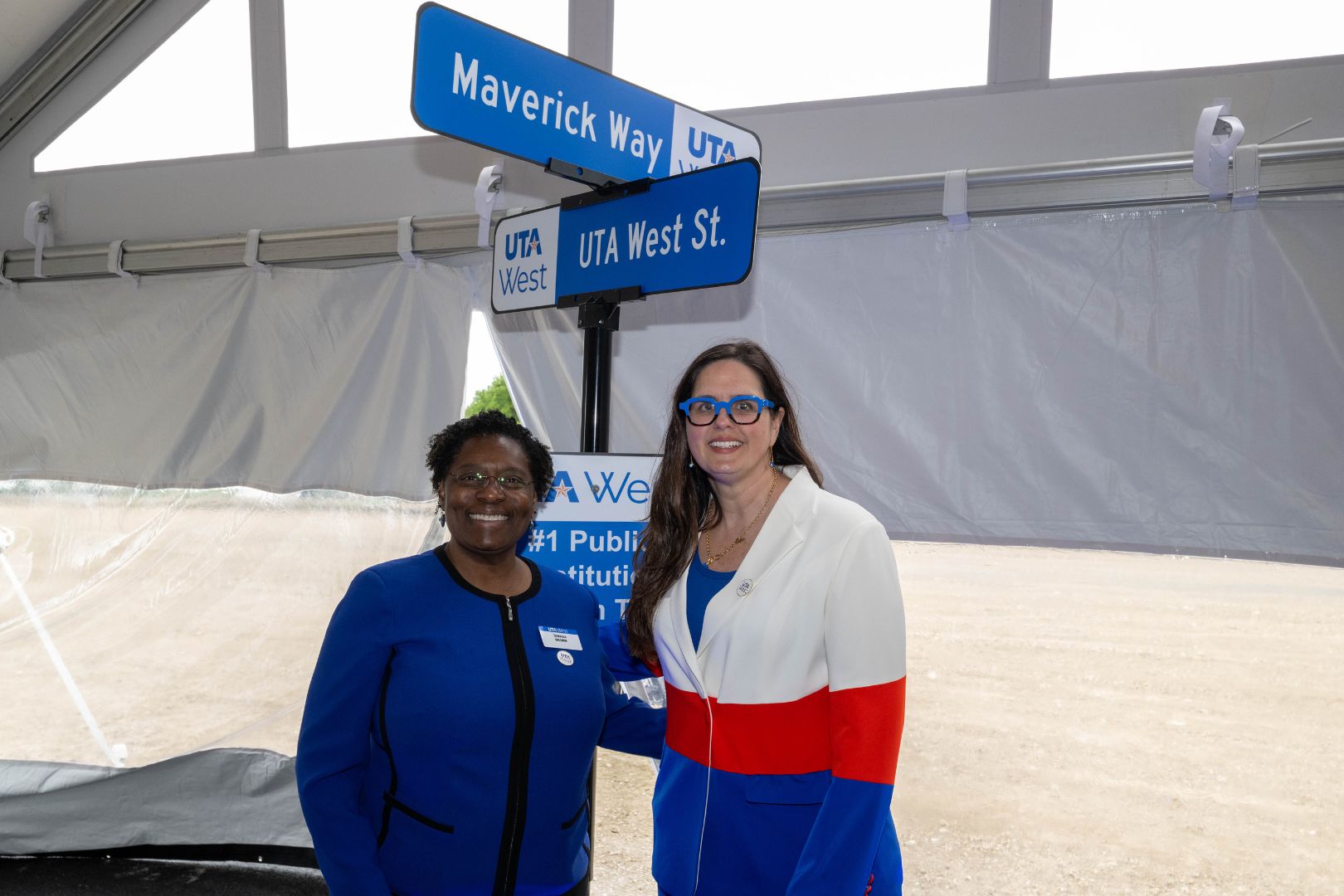 Image shows UTA President Jennifer Cowley and Provost Tamara L. Brown pose for a photo in front of a UTA West sign