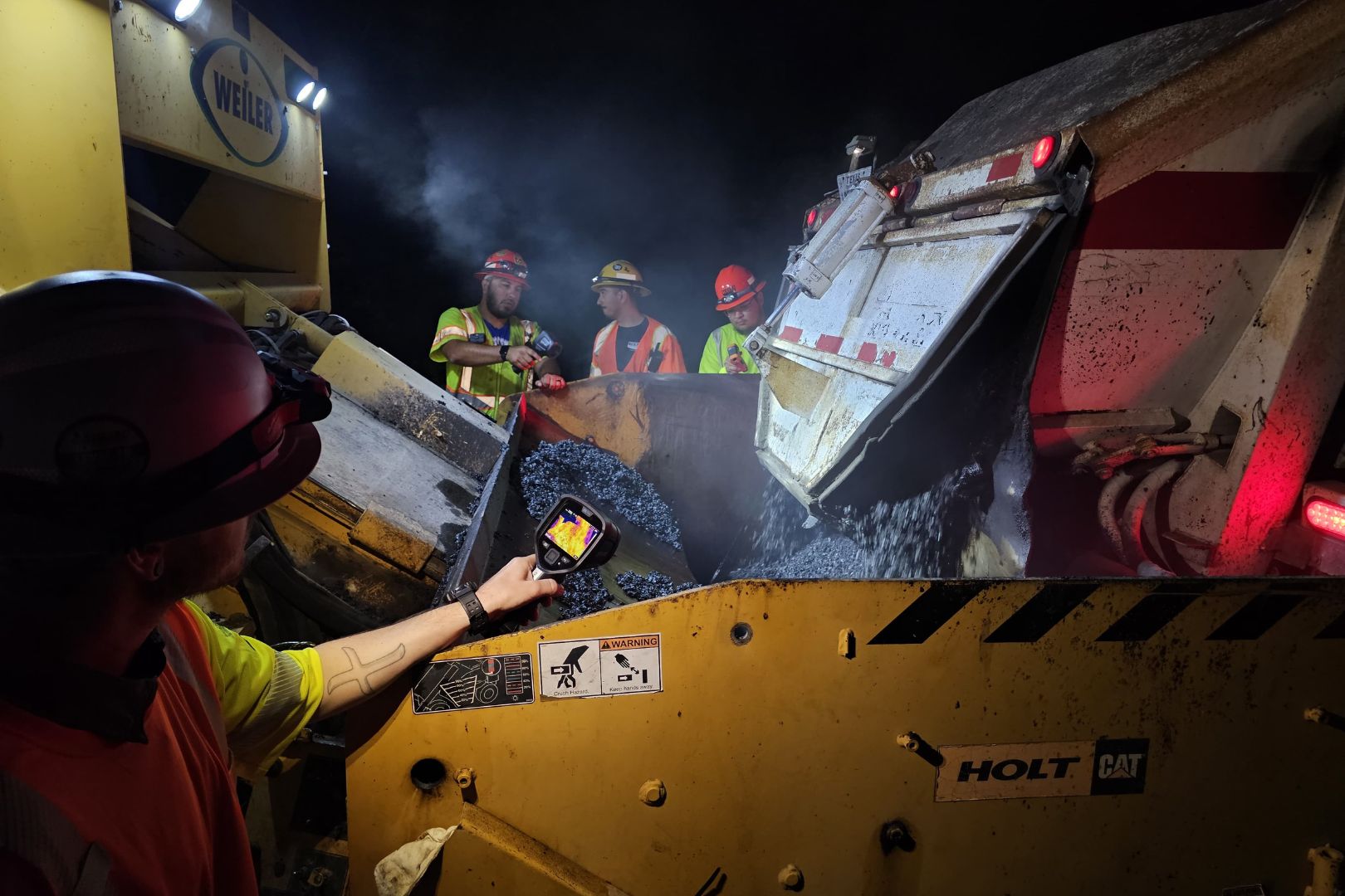 Image shows UTA students and faculty inspecting the plastic-infused asphalt as it gets poured