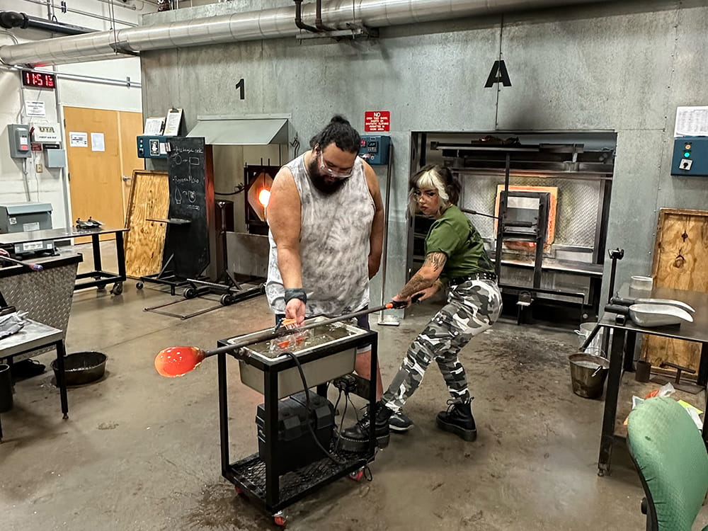 Two UTA students blow glass in the glass facilities.