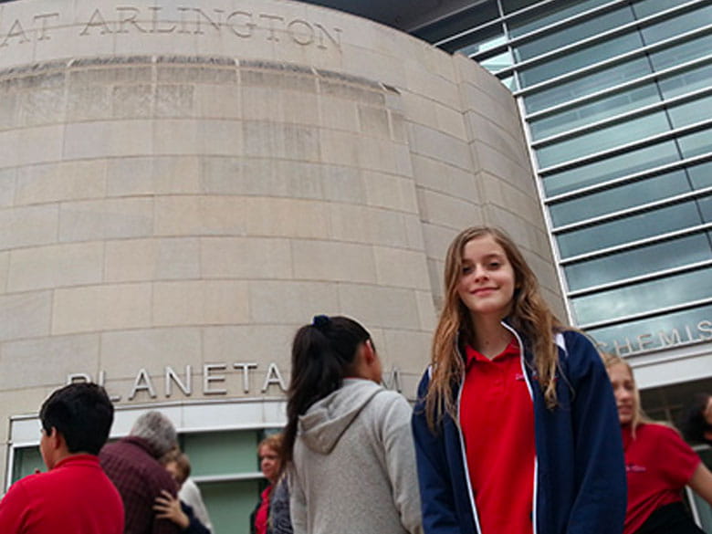 A student member of a class field trip smiles at the camera outside the UTA Planetarium.