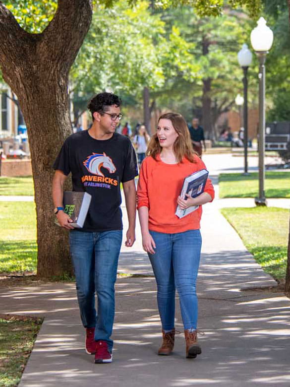 Two students walk through the quad at UTA carrying books.