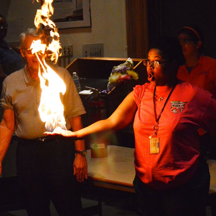 Liquid soap in a student's hand is lit on fire in a demonstration for other students during a UTA Science Ambassadors show.