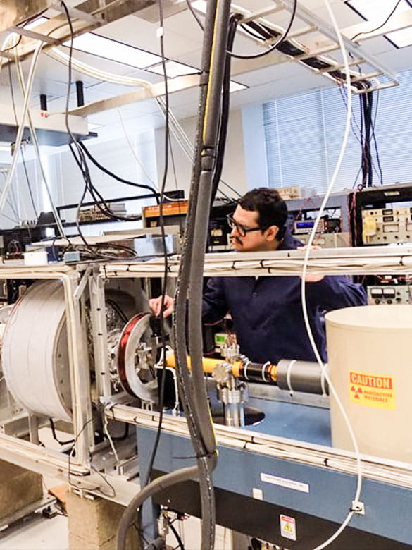 Graduate student Edward Perez closing valve to the cryogenic positron moderator system.  A 22Na Source emits positrons at high energies.  The positrons are slowed down using a solid neon moderator system (far right).