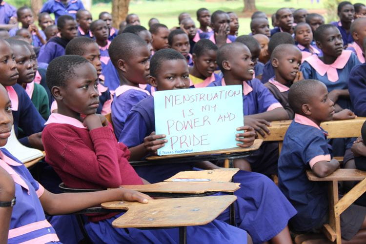 Kenya student in class holding a sign that say "Menstruation is my Power and Pride"