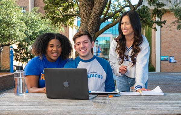 Three UTA students sitting at a table looking at a laptop