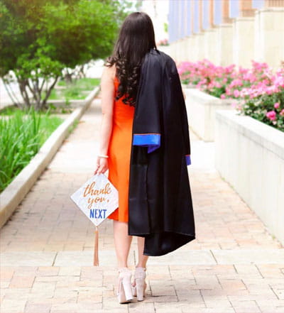 A UTA student walking away with graduation gown and cap in her hand 
