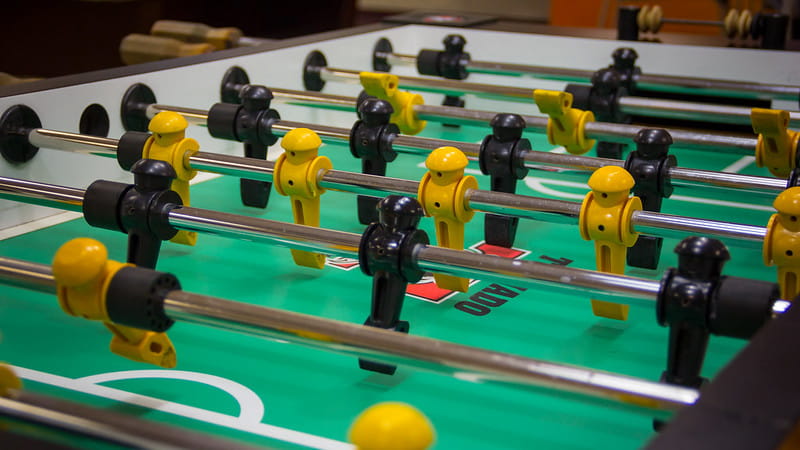 Close up shot of a Foosball table with yellow and black foosball players on rods.