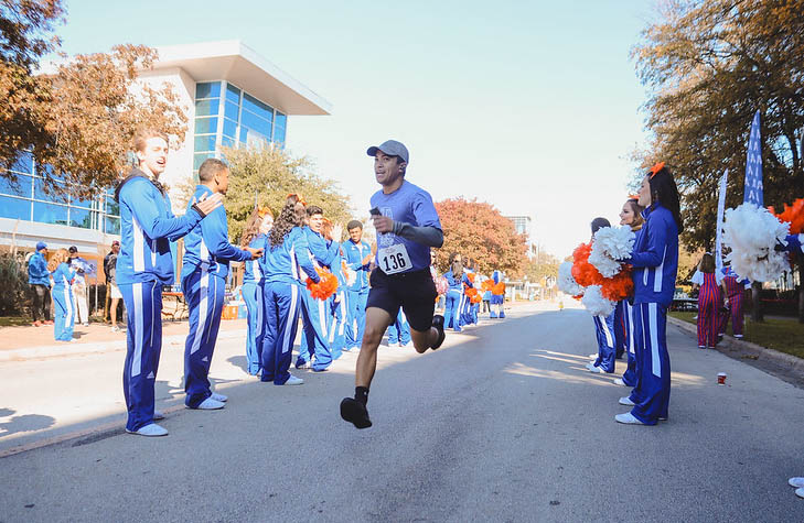 5K participant running towards the finish line as volunteers cheer him on