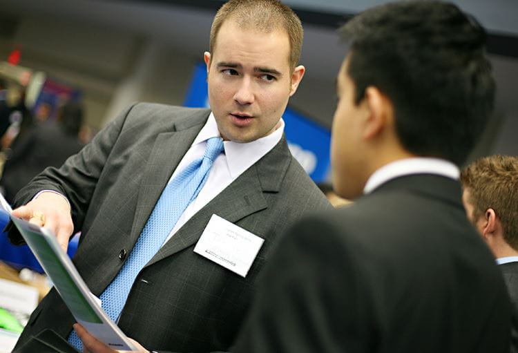 man with file talking to student in suits