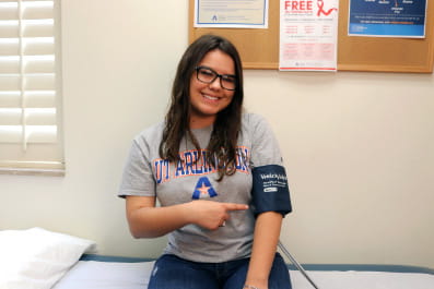A student smiling and pointing to a sphygmomanometers on arm