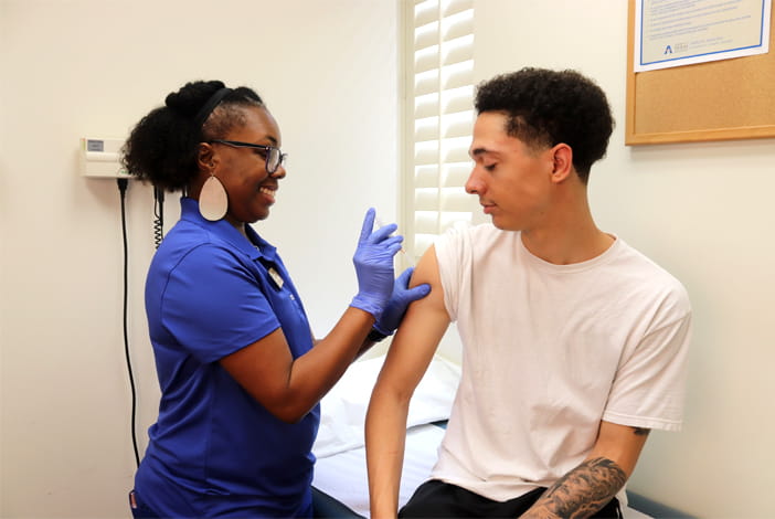 A male student getting a shot from a smiling health professional.