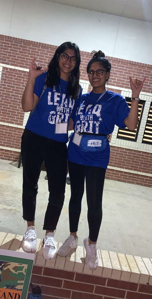 Two female business students holding up thumb and pinky in maverick salute.