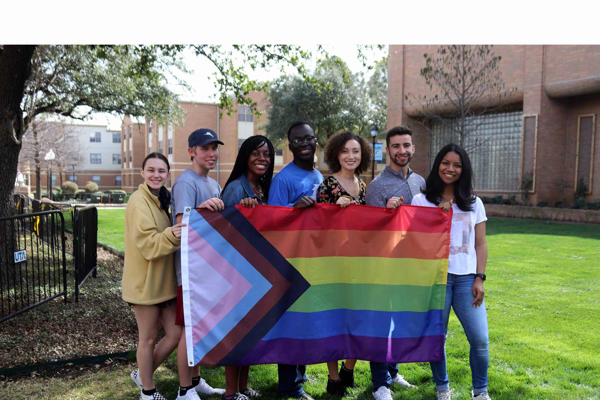 7 students holding the lgbtqa+ flag outside