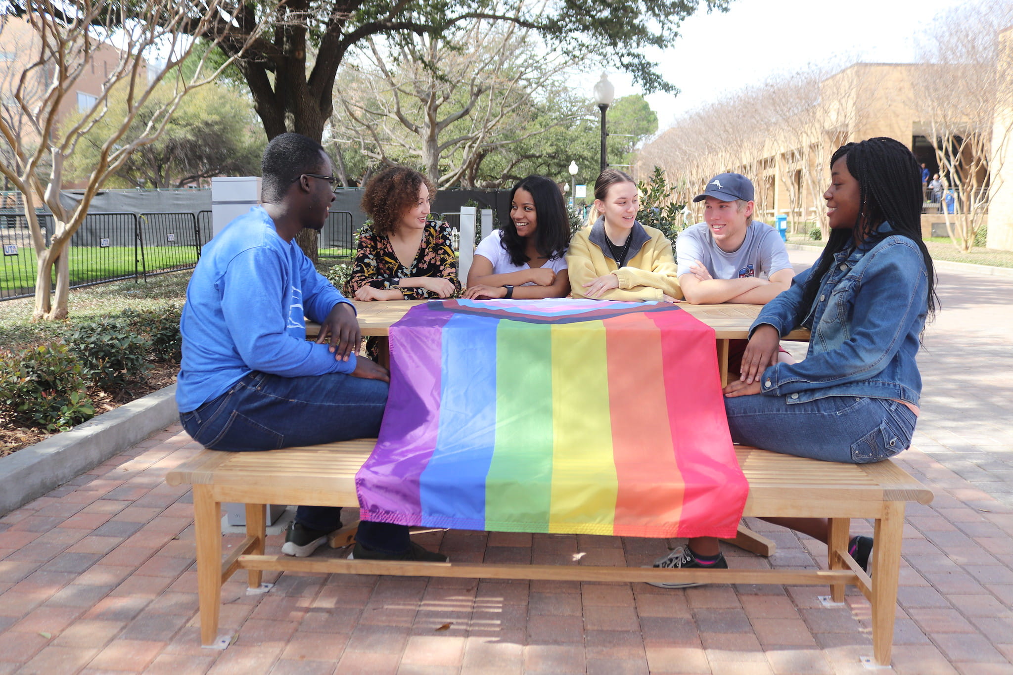 UTA students sit around a table that is covered with a pride flag at UTA