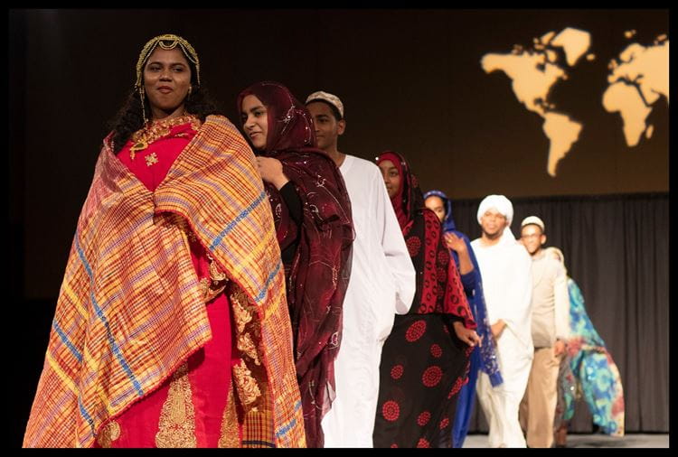 A group of students walking down the stage in their cultural clothing