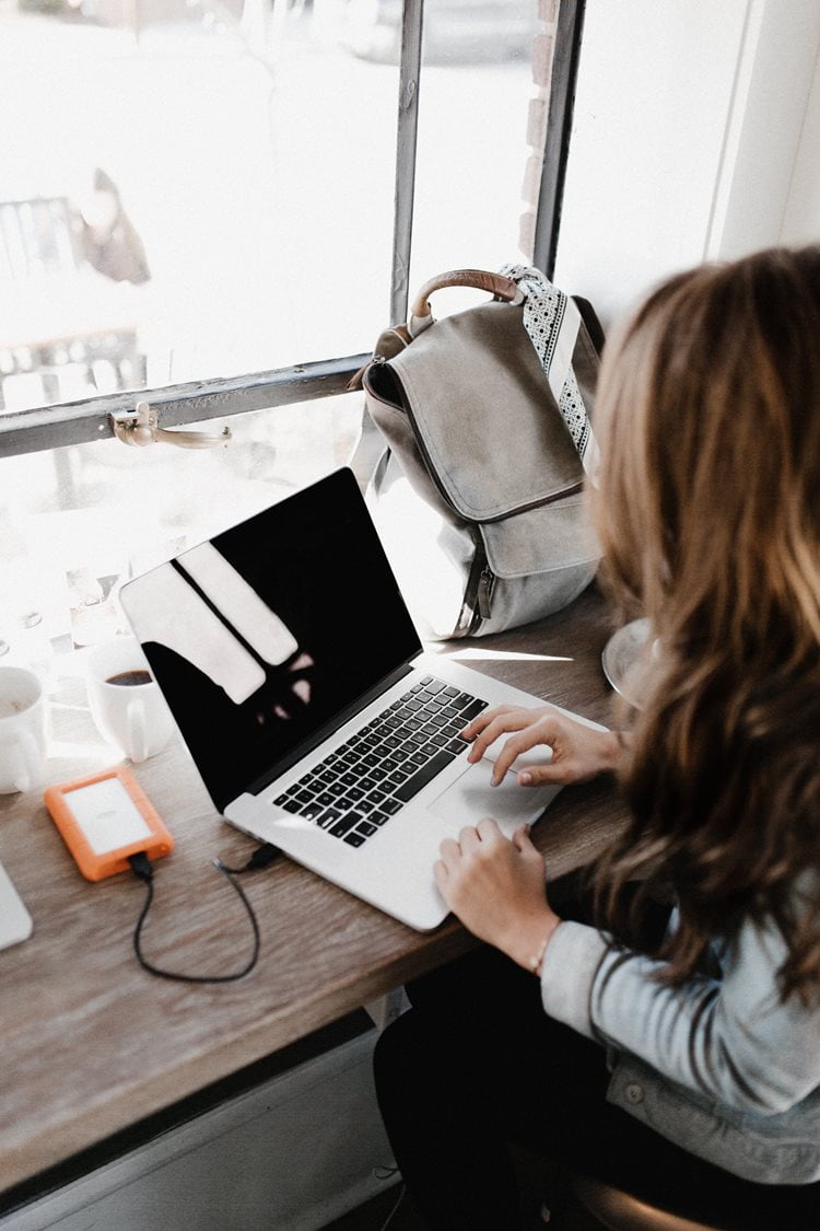 Person with long hair sitting at a desk with their laptop