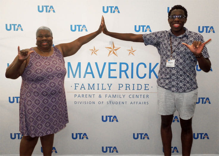A mother and son high fiving in front of a sign that says "Maverick Family Pride."