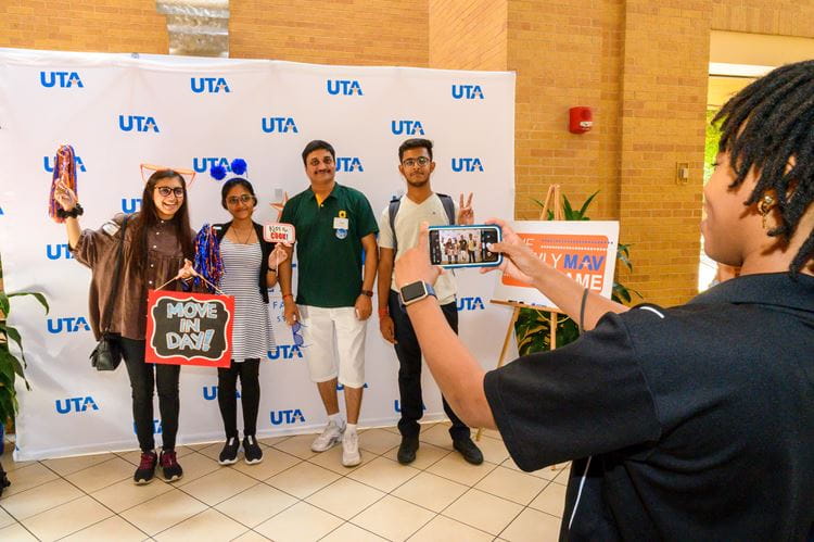 Family getting their picture taken in front of a backdrop with uta labels on it