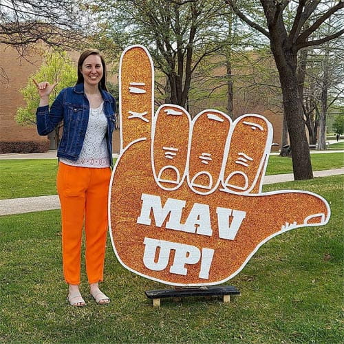 Woman standing next to a giant hand stating "MAV UP!" while mavving up