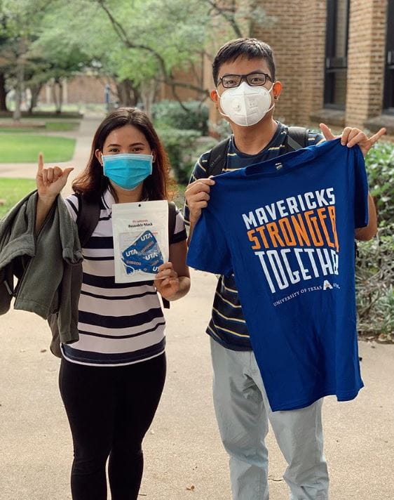 Two students wearing masks and holding up UTA swag.