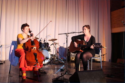 A band playing comprised of one woman with a bass and the other singing with a guitar