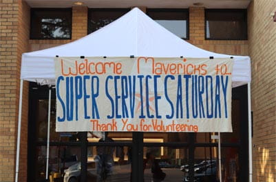 A tent holding up a sign labeled 'Welcome Mavericks to SUPER SERVICE SATURDAY Thank You for Volunteering'